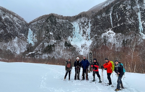 米子大瀑布と書かれている標柱と米子不動滝をバックに記念撮影するスノーシューハイキングツアーの参加者