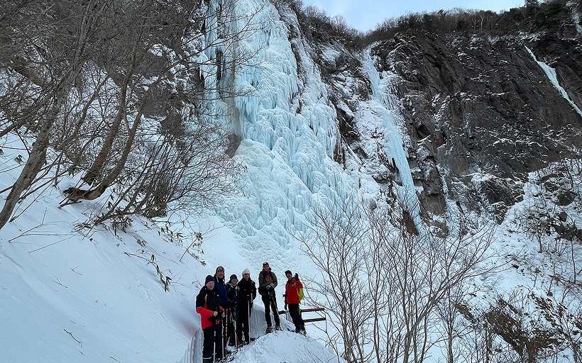 不動滝のすぐそばで記念撮影するスノーシューハイキングツアーの参加者