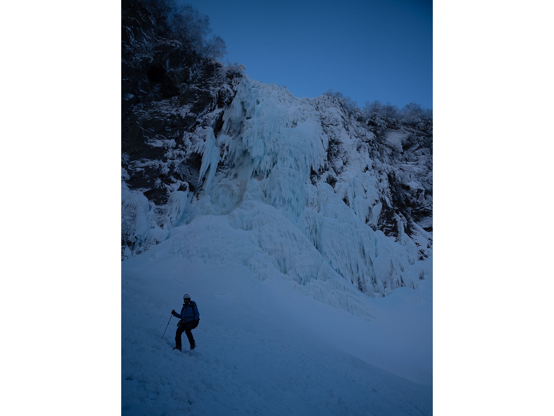 凍って神秘的な不動滝のすぐ側を歩く登山ガイド